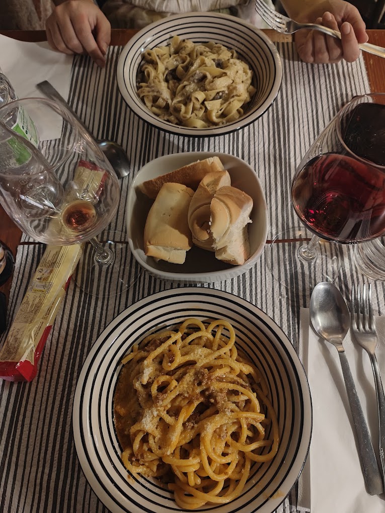 Tagliatelle ai funghi e bigoli al ragù in tavola all'Osteria La Vela, con pane e vino rosso
