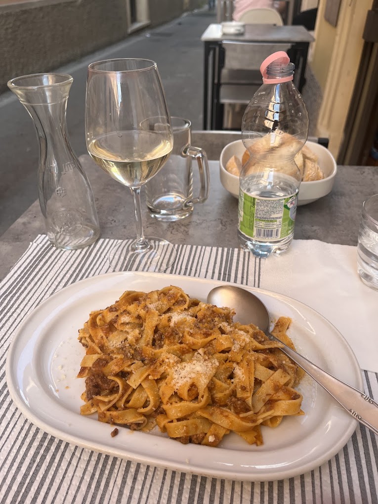 Tagliatelle al ragù e un calice di vino bianco al tavolo esterno dell'Osteria La Vela